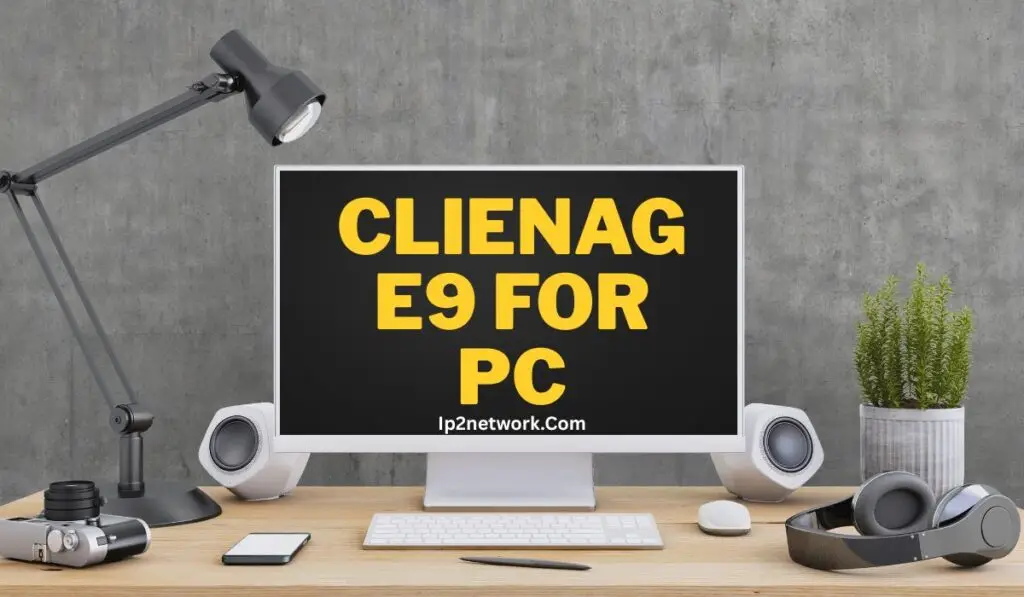 A modern computer setup on a wooden desk with a large monitor displaying the text “CLIENAGE9 FOR PC” in bold yellow letters and “Ip2network.Com” below it. The desk also has a lamp, speakers, camera, smartphone, keyboard, mouse, headphones, and a small potted plant against a gray concrete wall background.